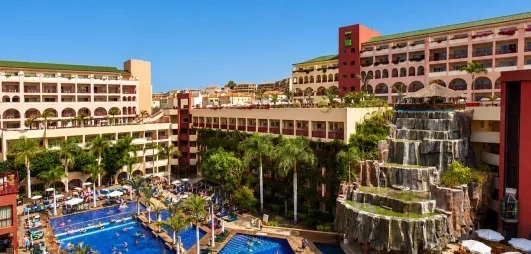 Un complexe hôtelier moderne avec plusieurs piscines entourées de palmiers et de chaises longues.