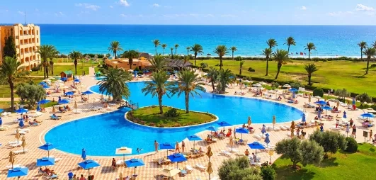 Grande piscine lagune entourée de palmiers et transats au club de vacances Nour Palace Mahdia en Tunisie.