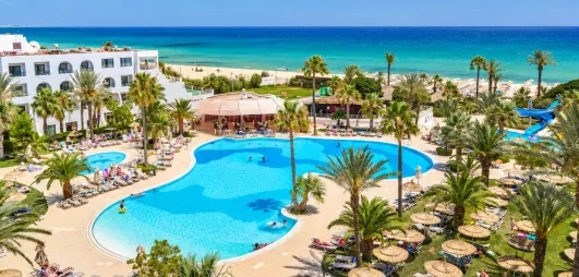 Vue panoramique sur la piscine lagune du Mondi Club Nozha Beach à Hammamet avec palmiers, transats et vue sur la mer Méditerranée.