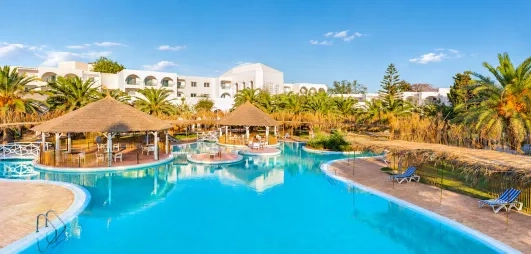 Grande piscine lagon du Mondi Club Shalimar Hammamet bordée de palmiers et d'aillottes en paille.