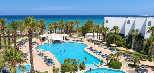 Vue aérienne de la grande piscine extérieure du Mondi Club Thalassa Mahdia entourée de palmiers avec la mer Méditerranée en arrière-plan à Mahdia en Tunisie.