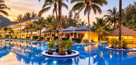 Une large piscine entourée de palmiers et de jardins tropicaux au coucher du soleil.