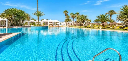 Grande piscine extérieure entourée de palmiers et de transats sous le soleil au Djerba Golf.