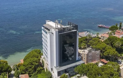 Une vue aérienne plongeante d'un hôtel moderne bordant une eau turquoise cristalline.