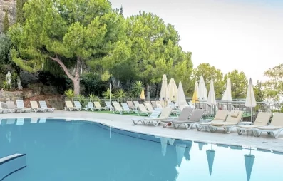 Une piscine aux eaux turquoise bordée de transats et de végétations verdoyants. 