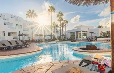 vue sur la piscine  avec transats et palmiers et coucher de soleil