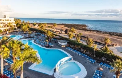Un panorama ensoleillé montrant une piscine, nichée entre des bâtiments d'hôtel et la mer.