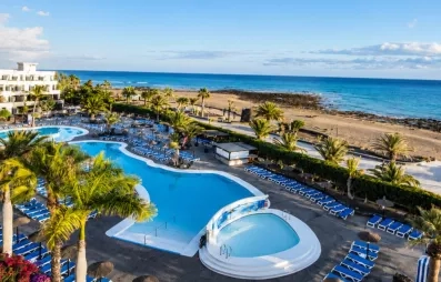 Un panorama ensoleillé montrant une piscine, nichée entre des bâtiments d'hôtel et la mer.