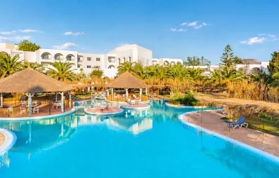 Grande piscine lagon du Mondi Club Shalimar Hammamet bordée de palmiers et d'aillottes en paille.