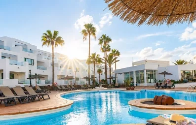 Une vue panoramique d'une grande piscine, bordée de transats et de bâtiments blancs modernes.
