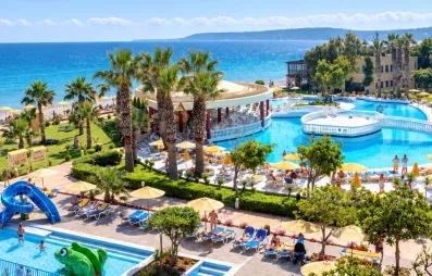 vue aérienne piscines, petit toboggan dans la piscine enfant, palmiers, pont et plateforme sur la piscine adulte, accès plage de galets, pieds dans l'eau, transats 