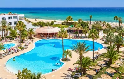 Vue panoramique sur la piscine lagune du Mondi Club Nozha Beach à Hammamet avec palmiers, transats et vue sur la mer Méditerranée.