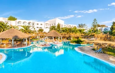 Grande piscine lagon du Mondi Club Shalimar Hammamet bordée de palmiers et d'aillottes en paille.