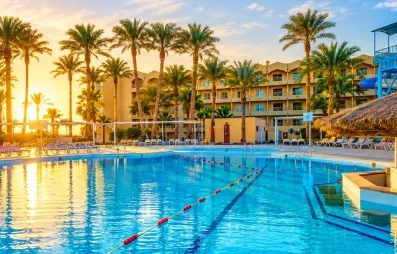 vue piscine extérieur avec bar central, transats autour, coucher de soleil, palmier, bâtiment de l'hôtel