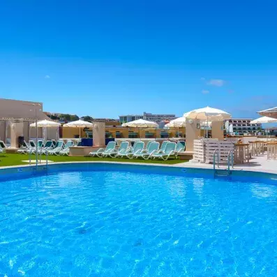 Une piscine sous un ciel bleu, bordée de nombreux transats et parasols blancs.