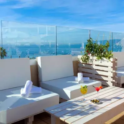 Une terrasse ensoleillée offrant des banquettes et une vue panoramique derrière une paroi en verre.