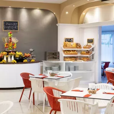 Un coin cafétéria avec des tables blanches, des chaises et des présentoirs de viennoiseries.