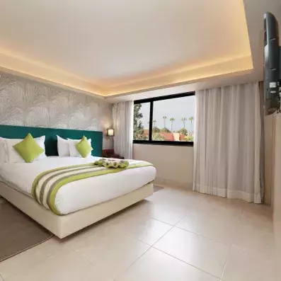 Chambre avec grand lit de deux places, tête de lit en vert, fenêtre à droite avec rideaux blancs 