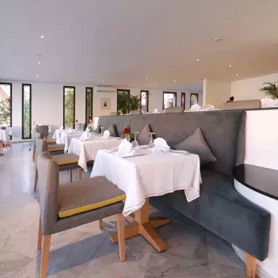 Le restaurant de l'hôtel avec des chaises grises et des tables avec des nappes blanches 