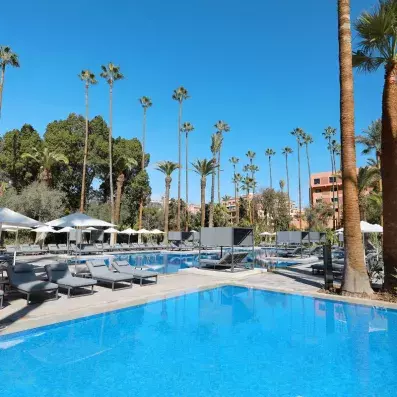 La piscine extérieur de l'hôtel et transats au bords avec des parasols et des palmiers