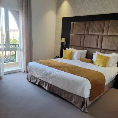 lit double avec une tête de lit en tissu et en bois marron et juste à côté une fênetre 