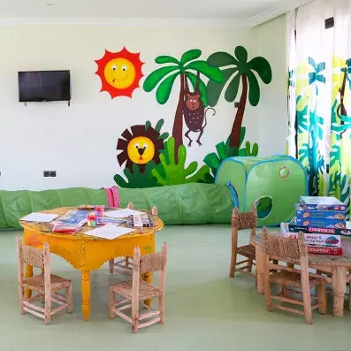 mini club enfant décoré par des palmiers au mur avec des petites tables/chaises et des jeux