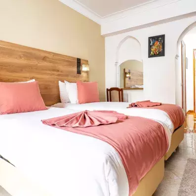 Chambre de l'hôtel avec deux lits collé en blanc et rose poudré et tête de lit en bois