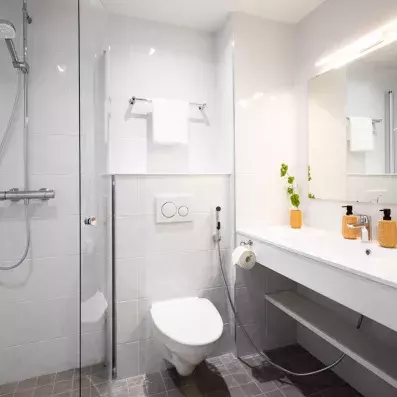 Salle de bain moderne et lumineuse de l'Hôtel Sodankylä avec douche à l'italienne, carrelage blanc et équipements contemporains.