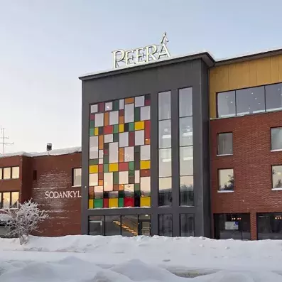 Façade extérieure de l'Hôtel Sodankylä sous la neige, bâtiment moderne avec vitraux colorés et enseigne lumineuse en Finlande.