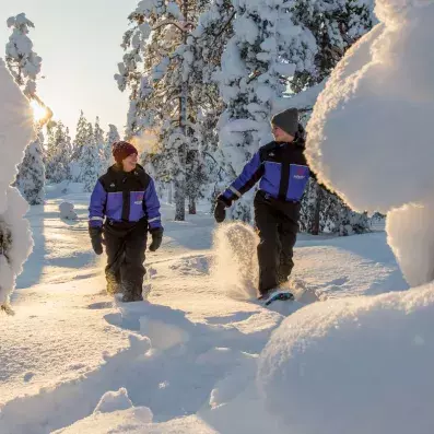 Couple profitant d'une balade en raquettes à neige dans la forêt boréale de Sodankylä au coucher du soleil.