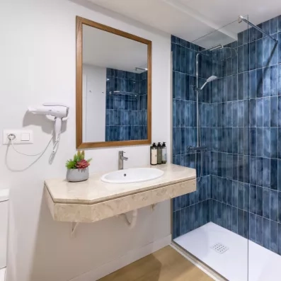 salle de bain aux couleurs bleues avec douche, évier, miroir et sèche cheveux 