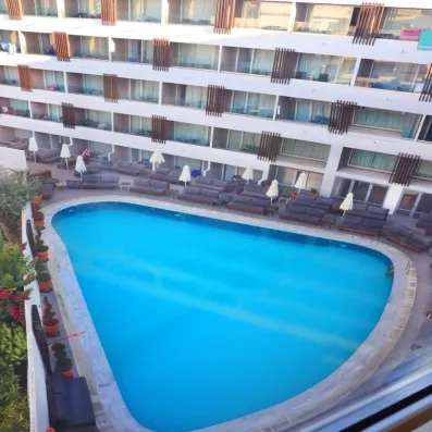 Vue générale de la piscine avec transats autour, palmiers, bâtiment de l'hôtel