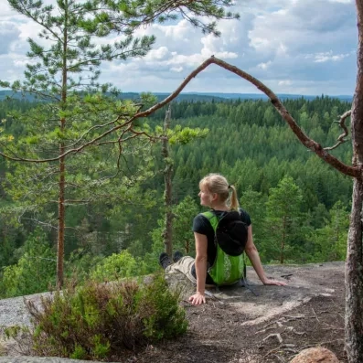 randonneuse assise sur un rocher en hauteur, au loin la foret finlandaise 