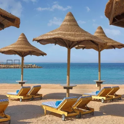 Transats et parasols sur la plage de sable de l'hôtel bord de mer Hilton Hurghada Plaza 5*.