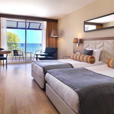 Une chambre avec deux lits simples et un balcon avec vue sur la mer.