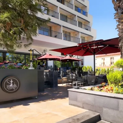 Vue de la terrasse de l'hôtel avec un bar extérieur couvert d'un parasol.