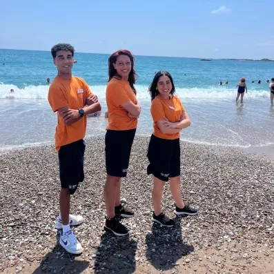 Trois animateurs posent sur la plage avec la mer en arrière plan.