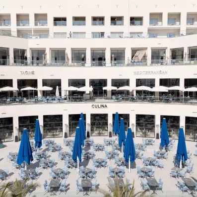 façade hôtel blanc étages parasol blancs au premier étage parasol et transat bleu au rdc