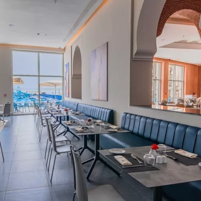 grande salle a manger tables et chaises grises banquettes bleues marine carrelage gris bleu foncé mur ouvert et grande baie vitrée vue terrasse extérieur meubles bleu parasols blancs