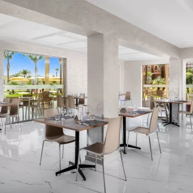 Restaurant avec grandes fenêtres qui donnent sur le jardin, tables et chaises 