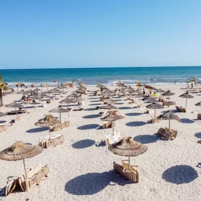 Une plage de sable fin bordée de parasols en paille, avec vue sur une mer turquoise, pour se détendre au soleil.