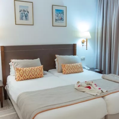 Une chambre lumineuse aux tons chaleureux, avec deux lits confortables et une décoration soignée aux touches orangées.