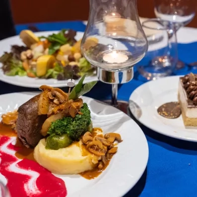 Un plat soigné mêlant viande, légumes et purée, accompagné d'une salade et d'un dessert, pour une expérience culinaire raffinée.