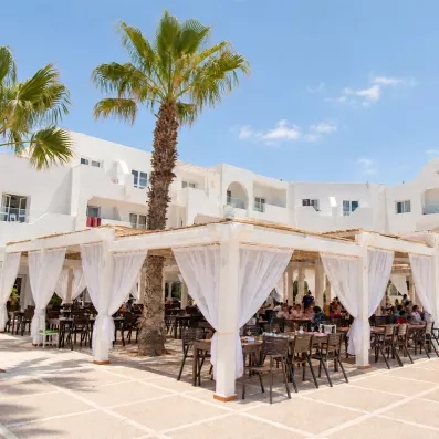 Terrasse extérieure du restaurant du Mondi Club Aladin Djerba avec palmiers et voilages blancs