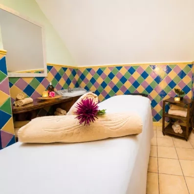 Une salle de soin avec une table de massage devant un mur de carreaux multicolores.