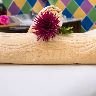 Un gros plan sur une table de massage préparée avec une serviette jaune et une fleur pourpre.