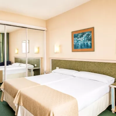 Une chambre d'hôtel sobre et lumineuse avec un grand lit double et un miroir mural.