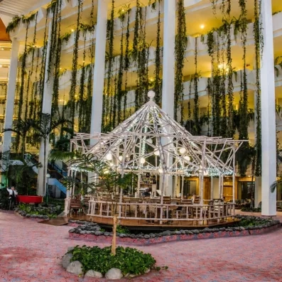 Un bar de jardin intérieur abrité sous une structure en verre et entouré de végétation.