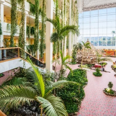 Un grand jardin d'hiver luxuriant avec de hauts palmiers et des allées fleuries.