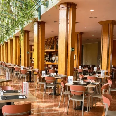 Un bar intérieur chaleureux avec de grandes colonnes en bois et de nombreuses tables.